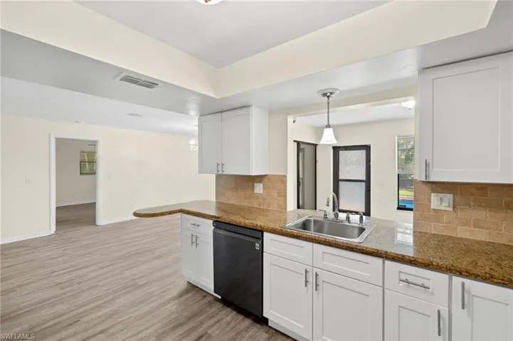 Kitchen featuring light wood finished floors, dishwasher, a sink, and white cabinets