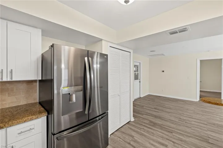 Kitchen featuring light wood-style floors, white cabinets, stainless steel refrigerator with ice dispenser, baseboards, and backsplash