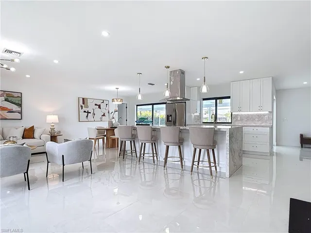 Kitchen with stainless steel fridge, a breakfast bar area, white cabinets, decorative backsplash, and hanging light fixtures