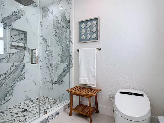Full bath with a marble finish shower and toilet
