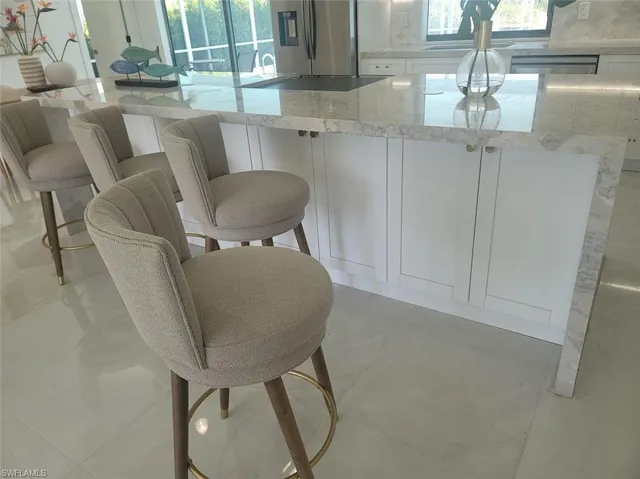 Kitchen featuring white cabinetry, light stone counters, stainless steel fridge with ice dispenser, and a kitchen bar