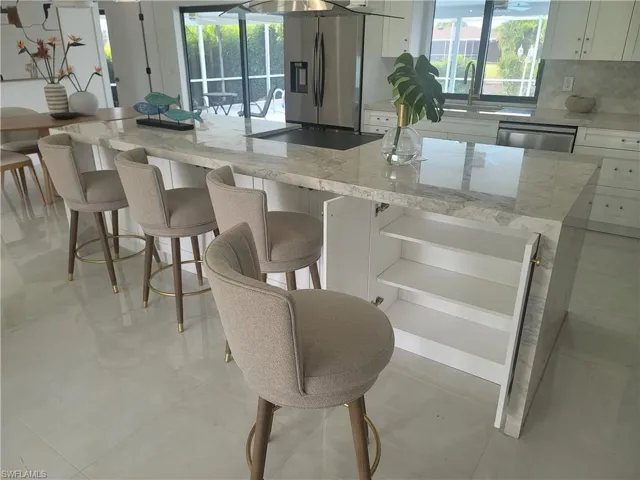 Kitchen with light stone countertops, white cabinetry, a kitchen island, and a kitchen bar