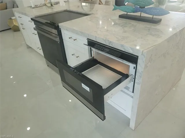 Kitchen with a warming drawer, light stone countertops, range with electric stovetop, white cabinetry, and light tile patterned floors