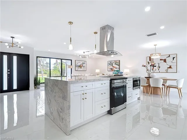 Kitchen featuring island exhaust hood, stainless steel electric range oven, white cabinetry, light stone countertops, and pendant lighting
