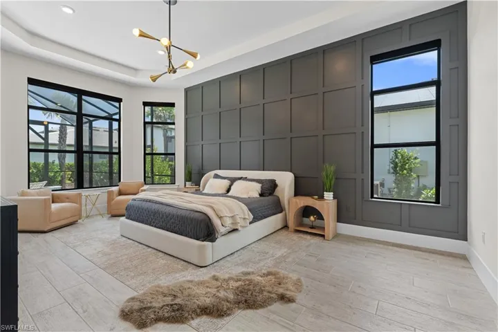 Bedroom with a decorative wall, light wood-type flooring, a chandelier, and a raised ceiling