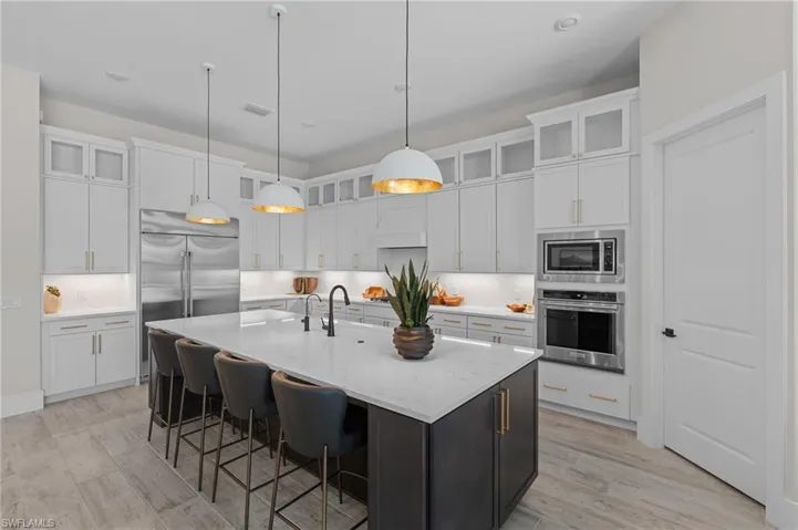 Kitchen with built in appliances, white cabinets, a large island, and pendant lighting