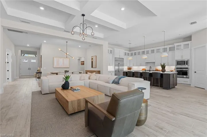 Living area with recessed lighting, an inviting chandelier, coffered ceiling, light wood-style flooring, and visible vents