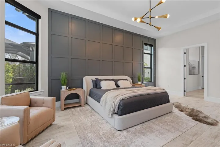 Bedroom featuring a chandelier, a decorative wall, multiple windows, and light wood-style flooring