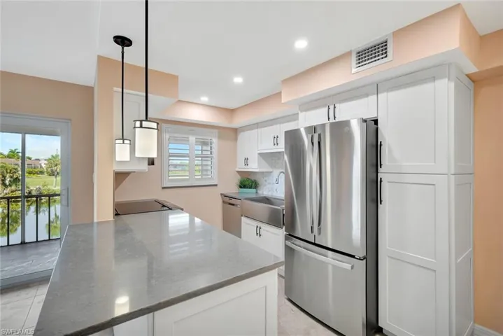 Kitchen featuring white cabinetry, stainless steel appliances, decorative light fixtures, decorative backsplash, and dark stone countertops