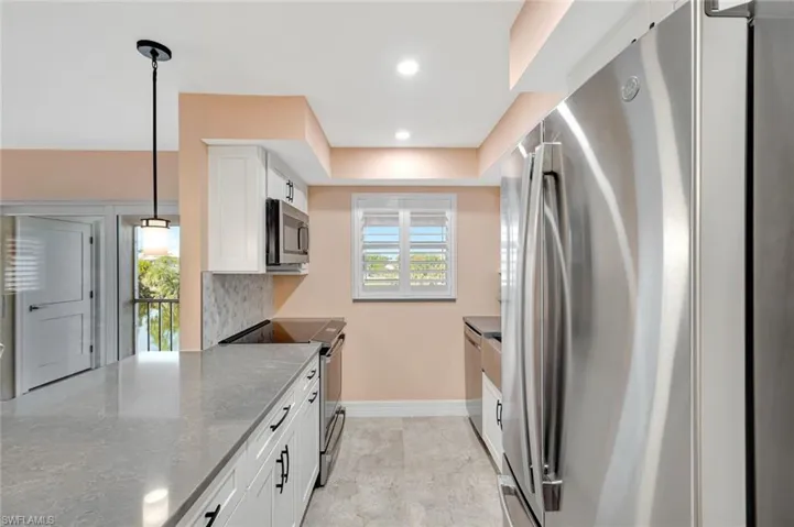 Kitchen with stainless steel appliances, white cabinets, decorative light fixtures, and plenty of natural light