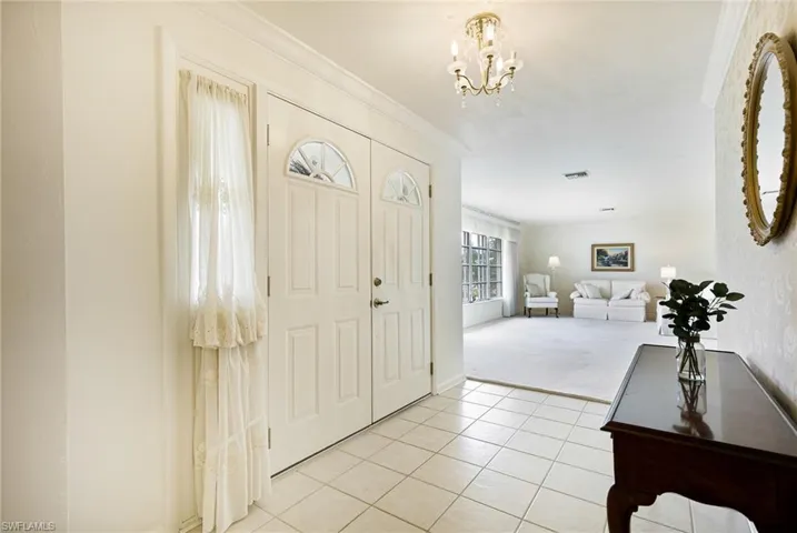 Foyer with light tile patterned floors, crown molding, a chandelier, and light colored carpet