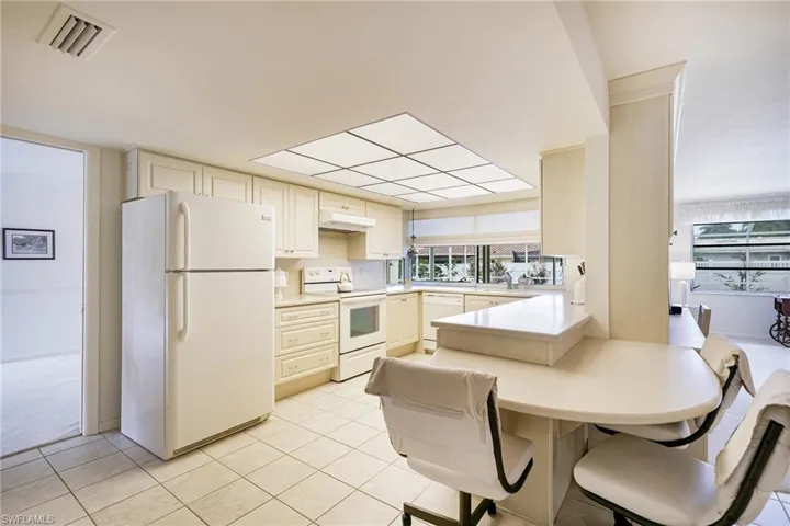 Kitchen with white appliances, a peninsula, cream cabinets, and light countertops