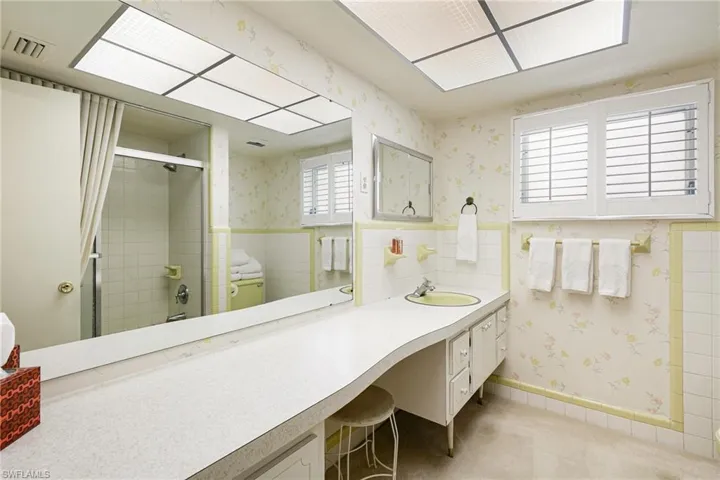 Bathroom with wallpapered walls, a tile shower, a wainscoted wall, and vanity