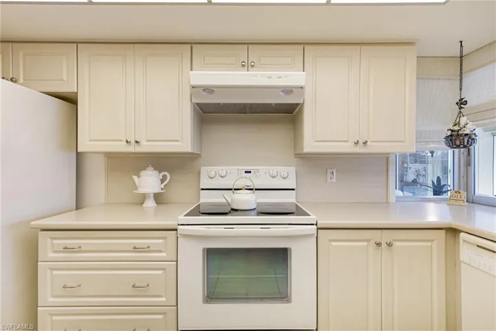 Kitchen featuring white appliances, under cabinet range hood, decorative backsplash, light countertops, and white cabinets