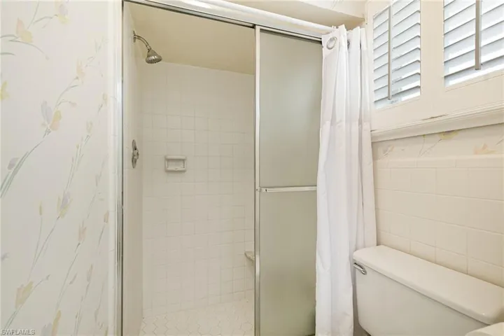 Bathroom featuring a shower stall, toilet, and tile walls