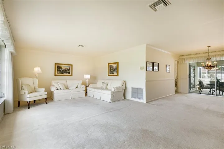 Carpeted living area with a chandelier, ornamental molding, and baseboards