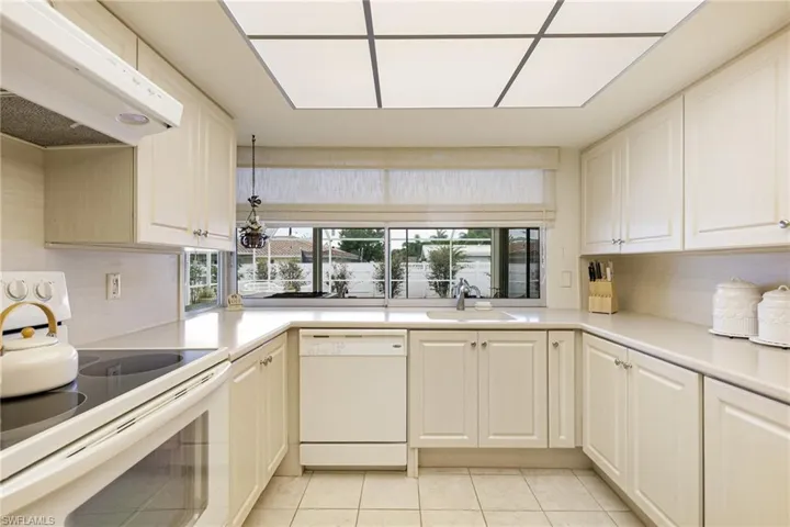 Kitchen featuring white appliances, under cabinet range hood, a sink, light tile patterned flooring, and light countertops