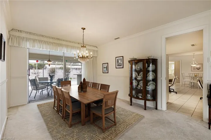 Dining space with light colored carpet, a chandelier, crown molding, and light tile patterned floors