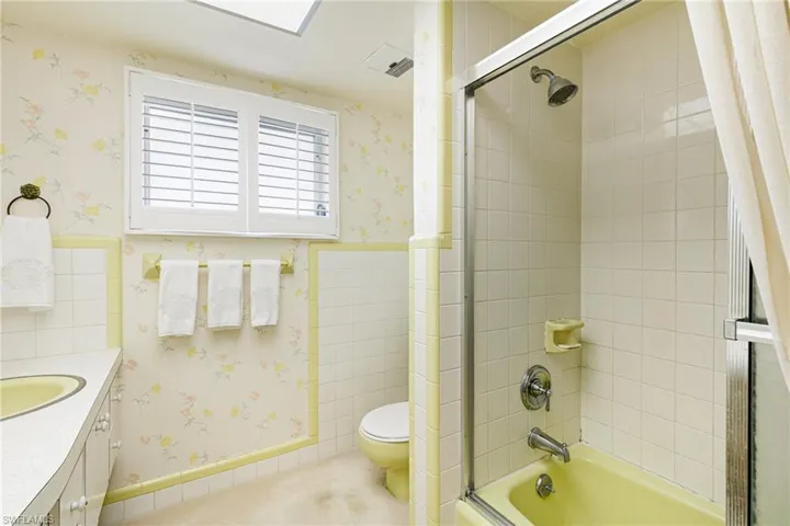 Bathroom with wallpapered walls, shower / tub combination, toilet, vanity, and wainscoting