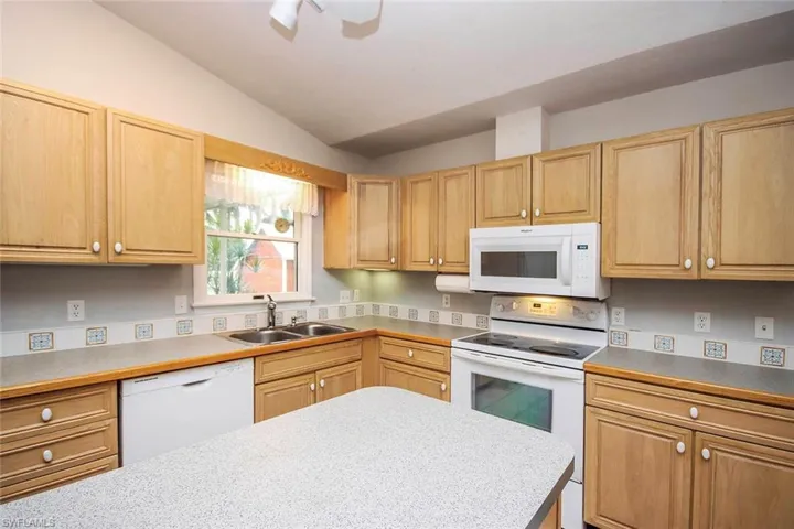 Kitchen featuring white appliances, light countertops, lofted ceiling, and light brown cabinets