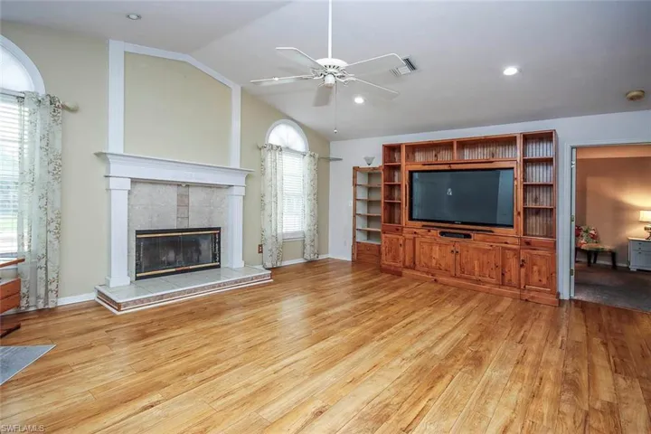 Unfurnished living room featuring a tiled fireplace, vaulted ceiling, light wood-style flooring, a ceiling fan, and recessed lighting