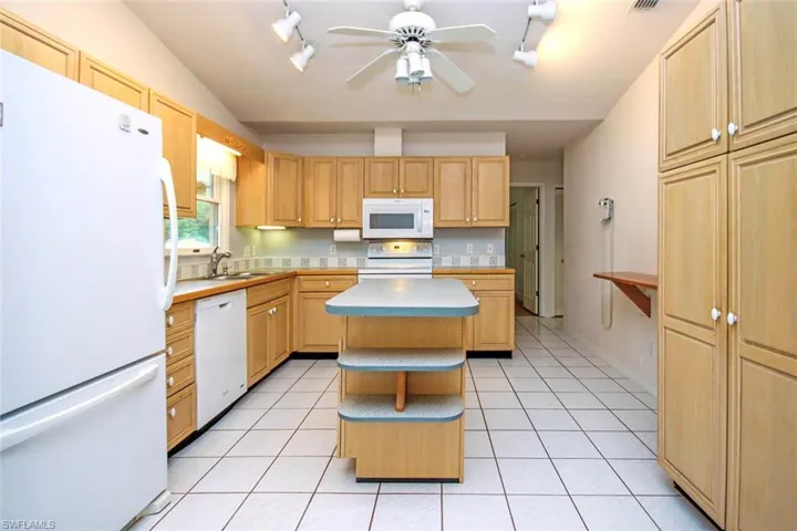 Kitchen featuring white appliances, a center island, light countertops, open shelves, and light tile patterned floors