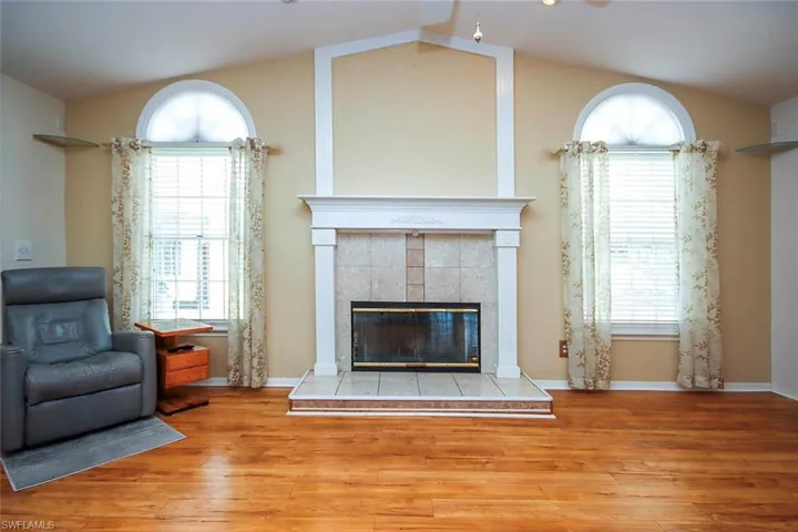 Living room with a tiled fireplace, wood finished floors, lofted ceiling, and ceiling fan