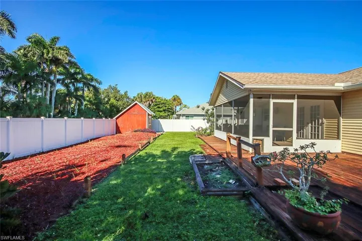 Fenced backyard featuring a sunroom, a vegetable garden, a shed, and a wooden deck