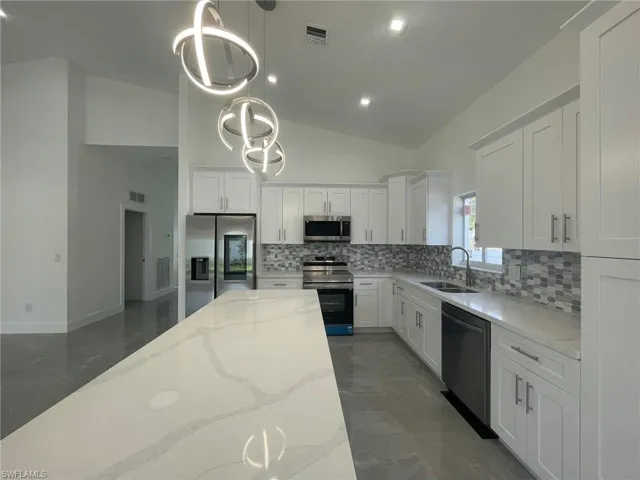 Kitchen featuring appliances with stainless steel finishes, backsplash, light stone counters, sink, and decorative light fixtures