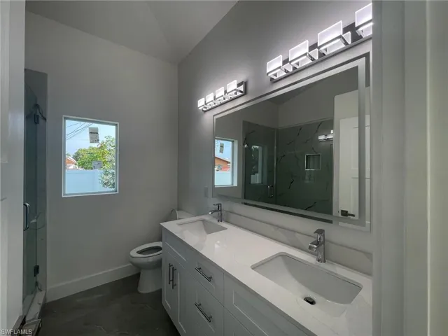 Bathroom with a shower with door, toilet, tile patterned floors, vaulted ceiling, and dual vanity