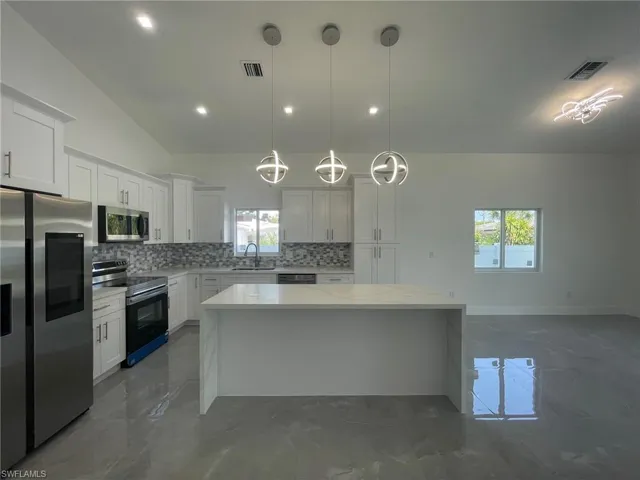 Kitchen featuring dark tile patterned flooring, pendant lighting, stainless steel appliances, backsplash, and plenty of natural light