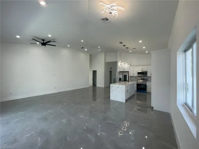 Unfurnished living room with ceiling fan with notable chandelier, tile patterned floors, and vaulted ceiling