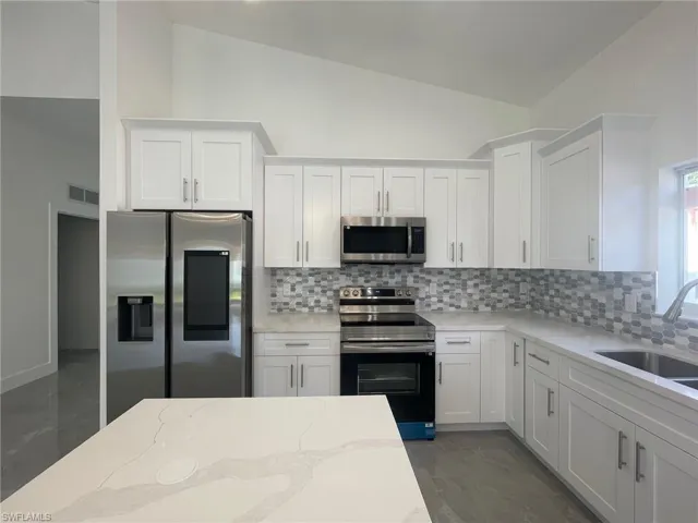 Kitchen with backsplash, appliances with stainless steel finishes, and white cabinetry