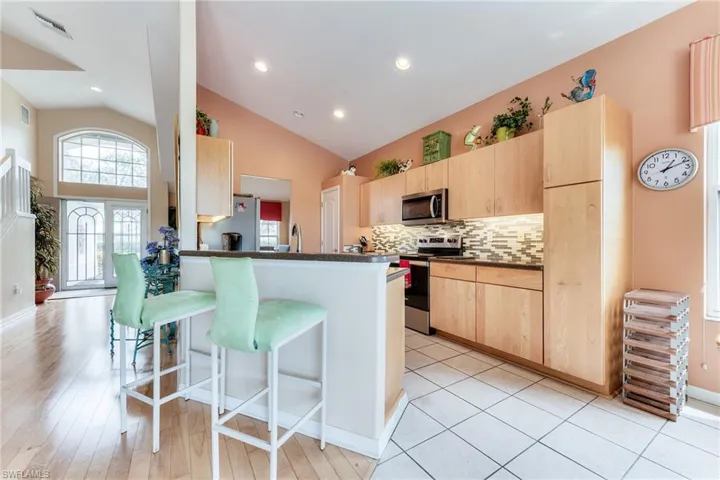Kitchen with dark countertops, a kitchen breakfast bar, a peninsula, stainless steel appliances, and light brown cabinets
