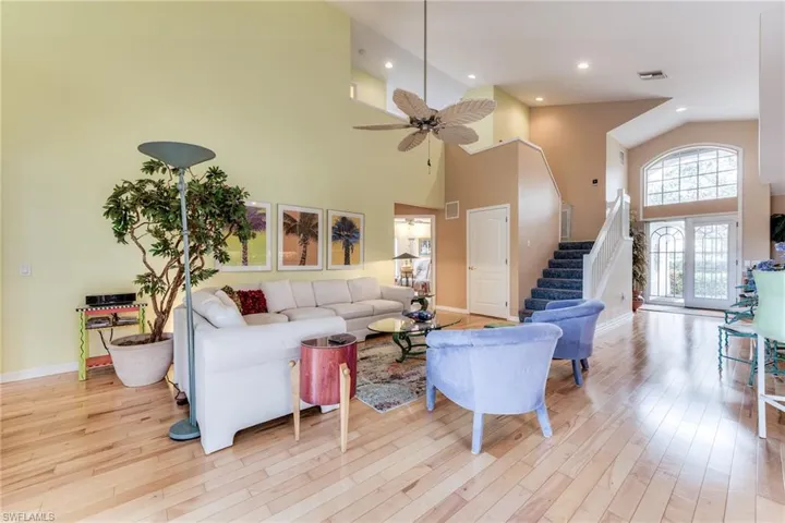 Living area featuring ceiling fan, high vaulted ceiling, visible vents, light wood-style floors, and stairway