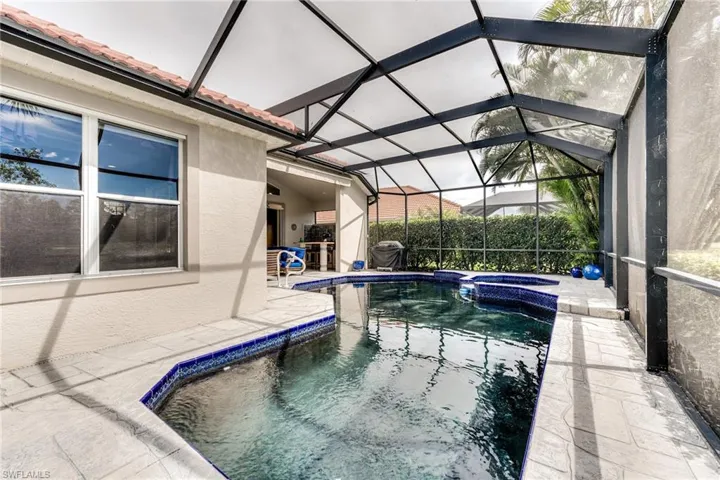 View of pool featuring glass enclosure, a patio area, and a pool with connected hot tub
