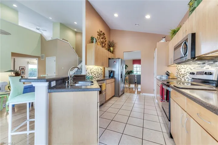 Kitchen with light tile patterned floors, a kitchen breakfast bar, stainless steel appliances, light brown cabinets, and a sink