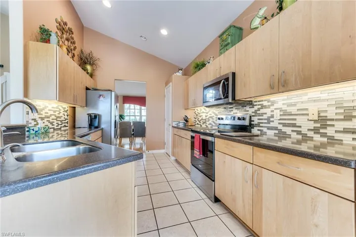 Kitchen featuring appliances with stainless steel finishes, light brown cabinets, vaulted ceiling, a sink, and light tile patterned flooring