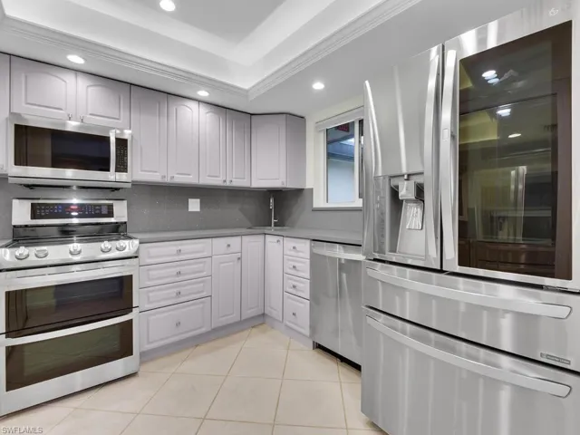 Kitchen featuring backsplash, white cabinetry, light tile patterned floors, and stainless steel appliances