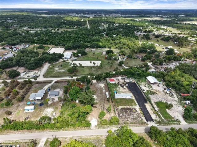 Expansive aerial showcasing a large parcel with a paved driveway and multiple structures, including a primary residence with an extended covered patio, a detached garage, and a separate outbuilding