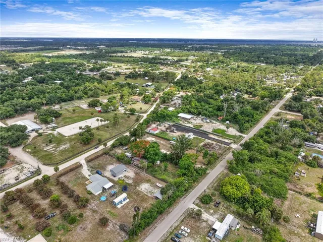 Aerial perspective showcasing a sprawling property with extensive cleared land, a distinct riding arena, multiple outbuildings, and mature landscaping
