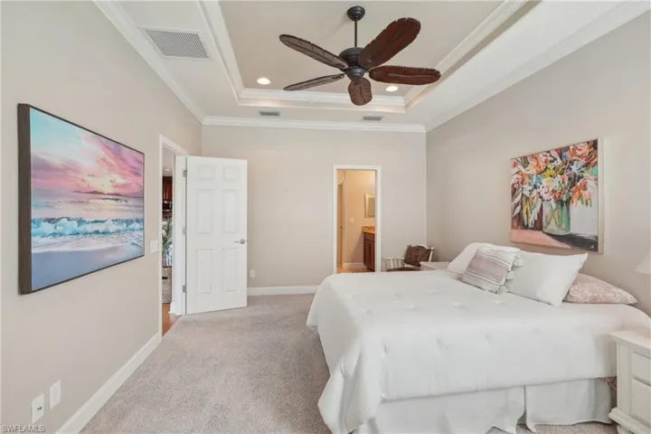 Bedroom with ensuite bathroom, crown molding, carpet flooring, a tray ceiling, and ceiling fan