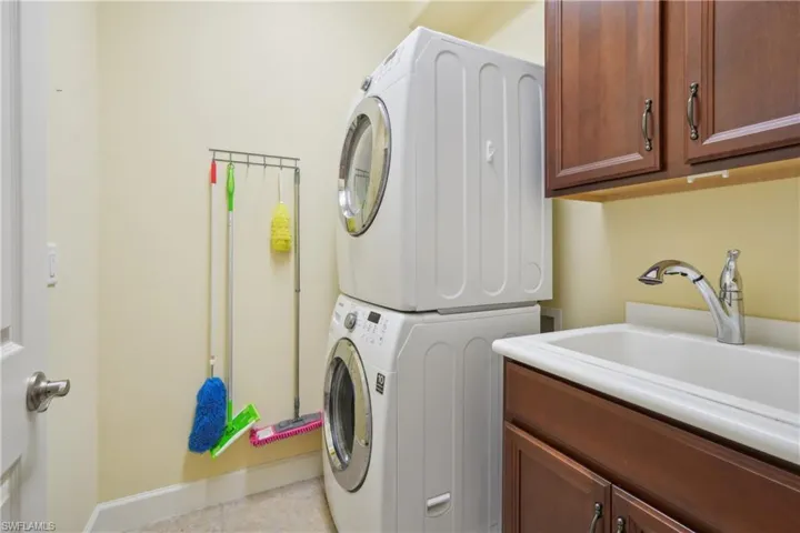 Washroom with stacked washer and clothes dryer, cabinets, sink, and light tile patterned floors