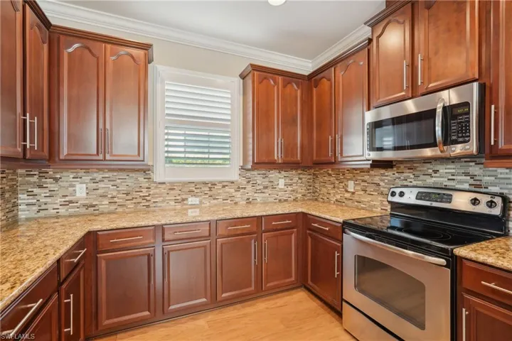 Kitchen with backsplash, light hardwood / wood-style flooring, appliances with stainless steel finishes, light stone countertops, and ornamental molding