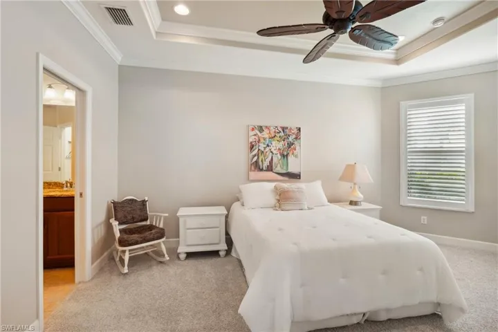 Bedroom with a raised ceiling, crown molding, connected bathroom, carpet flooring, and ceiling fan