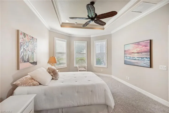 Carpeted bedroom featuring ceiling fan, a raised ceiling, and crown molding