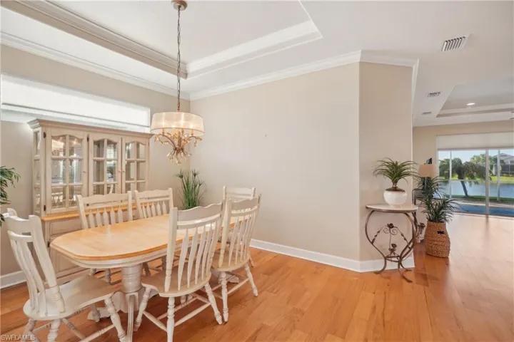 Dining area featuring light wood-type flooring, a tray ceiling, a chandelier, and crown molding