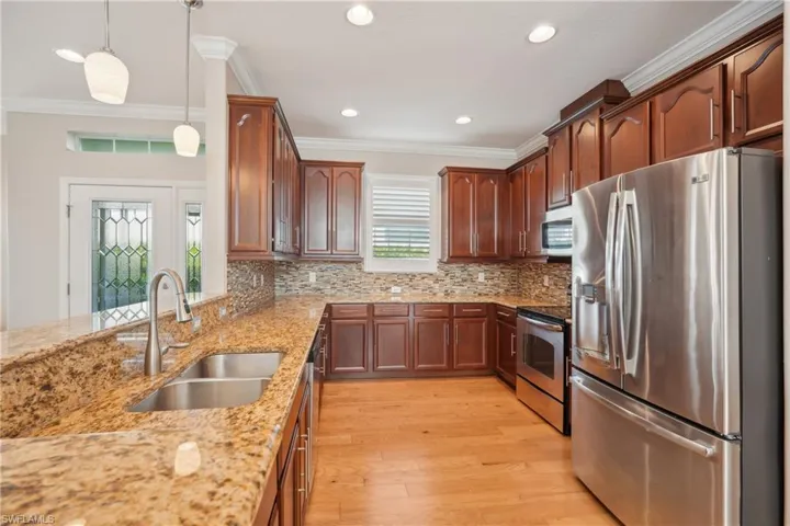Kitchen featuring light hardwood / wood-style flooring, decorative light fixtures, appliances with stainless steel finishes, sink, and ornamental molding