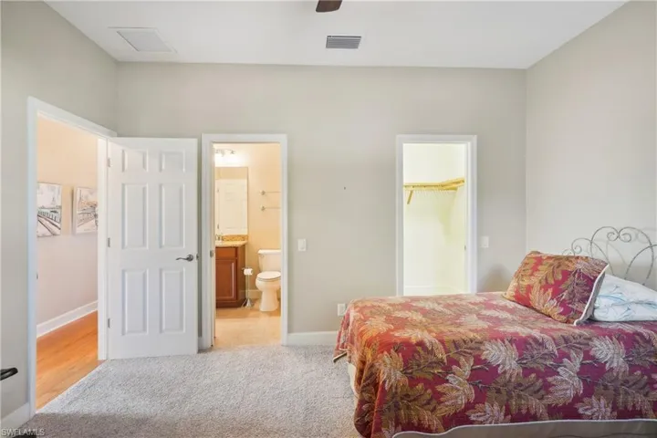 Carpeted bedroom with ensuite bath, a spacious closet, ceiling fan, and a closet