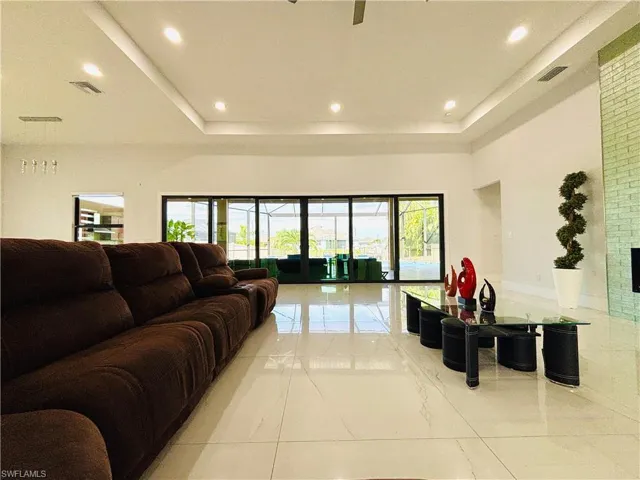 Living room featuring a tray ceiling, a ceiling fan, light marble finish flooring, and recessed lighting